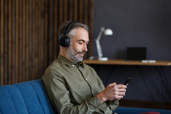 Senior Man In Headphones Listening Music On Smart Phone Using Mu