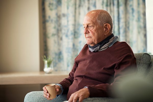 Depressed senior man sitting on armchair holding disposable cup