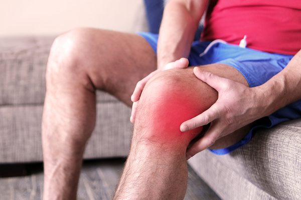 A Man On A Couch Clutching His Knee In Excruciating Pain. Joint