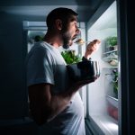 Hungry Man Eating Food At Night From Open Fridge. Man Taking Mid